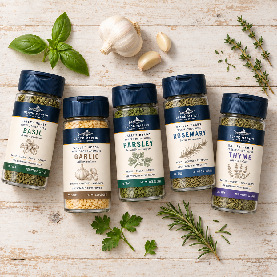 The Galley Starter: five Galley Herbs shaker jars - basil, garlic, parsley, rosemary and thyme - laid out on white-washed wood with fresh sprigs and garlic cloves