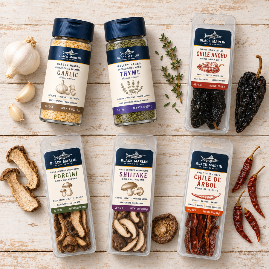 Two of Each: garlic and thyme shaker jars, porcini and shiitake mushroom packs, and ancho and chile de árbol packs, laid out on white-washed wood with whole dried chiles
